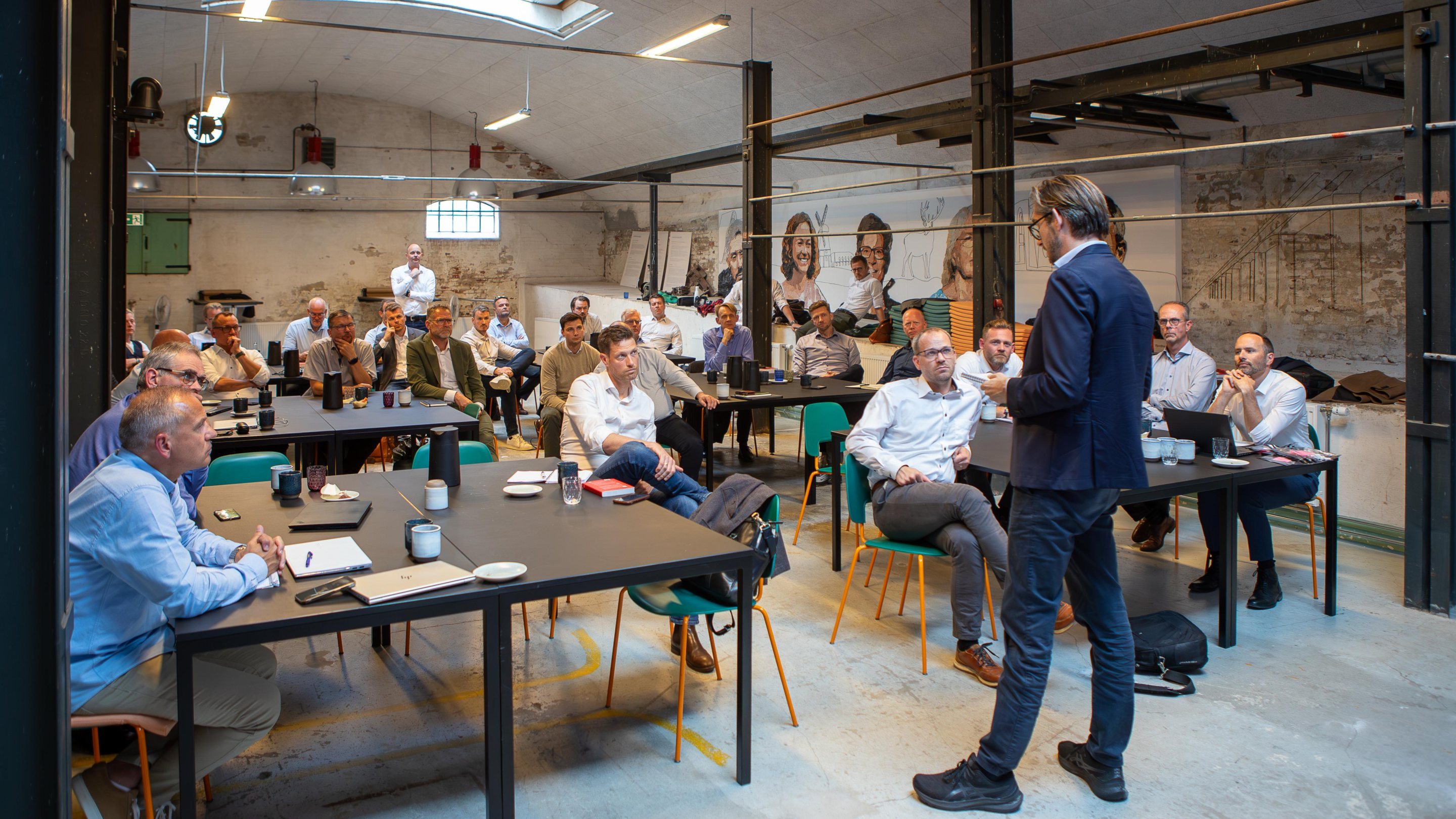 ZILLION consultants around the tables in a converted factory hall while a colleague leads the session